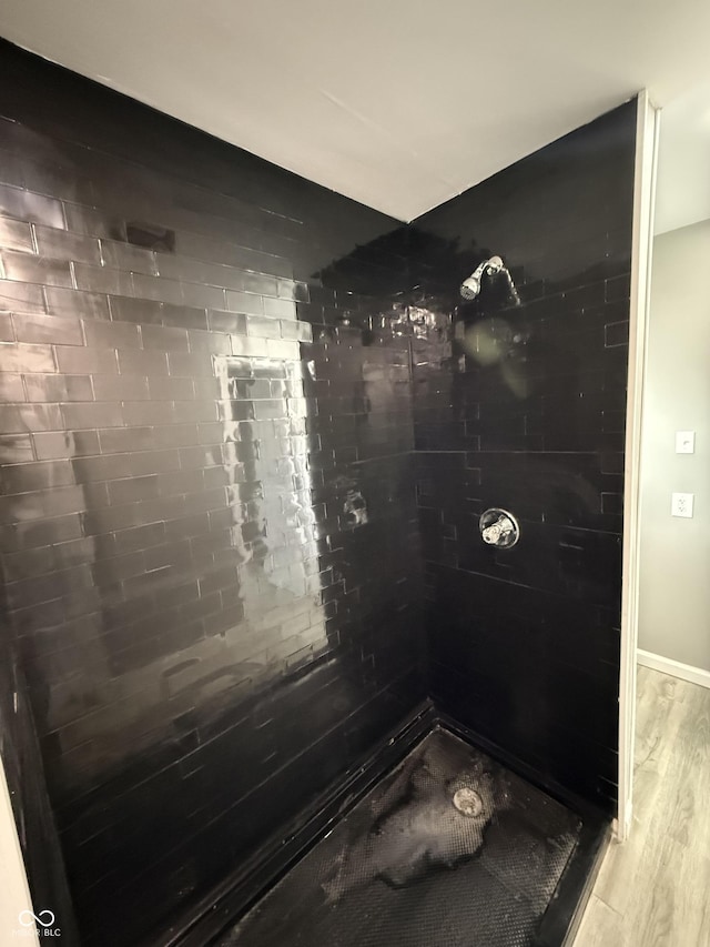 bathroom featuring baseboards, wood finished floors, and a tile shower