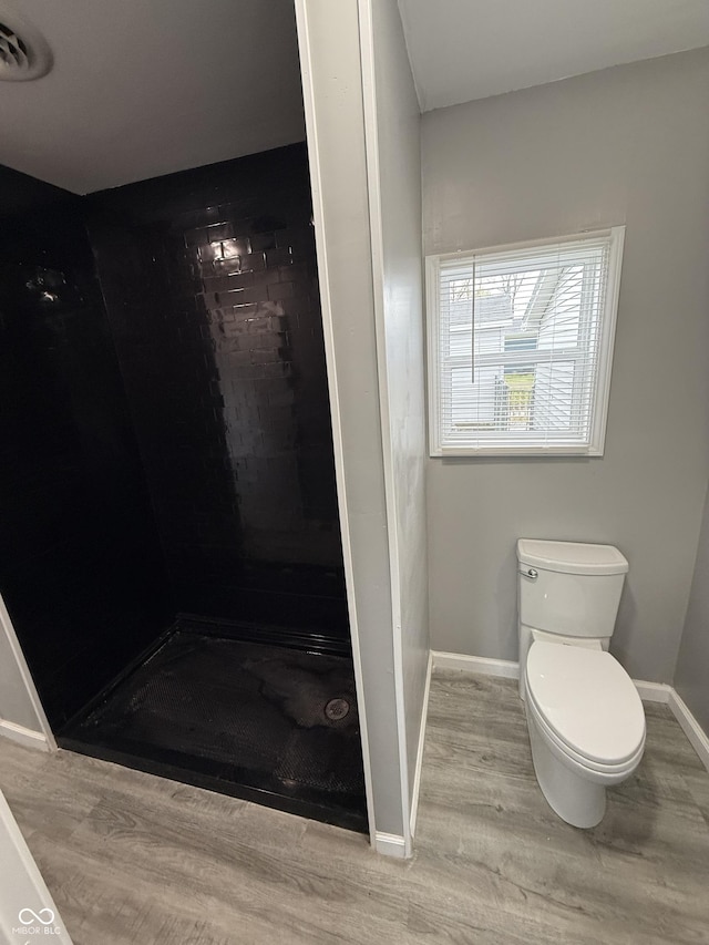 bathroom with toilet, a shower stall, wood finished floors, and baseboards