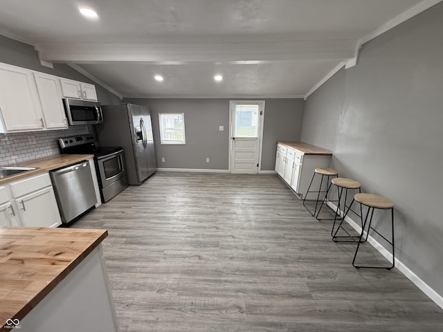 kitchen featuring butcher block counters, vaulted ceiling with beams, and stainless steel appliances