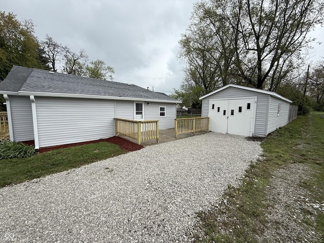 rear view of house featuring a wooden deck, a garage, a shingled roof, an outbuilding, and a storage unit