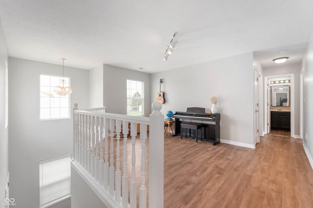 hallway featuring baseboards, a notable chandelier, light wood-type flooring, and an upstairs landing