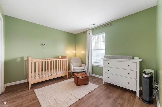 bedroom with visible vents, baseboards, wood finished floors, and a nursery area