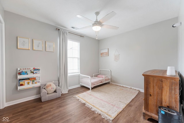 bedroom with baseboards, visible vents, a crib, and wood finished floors
