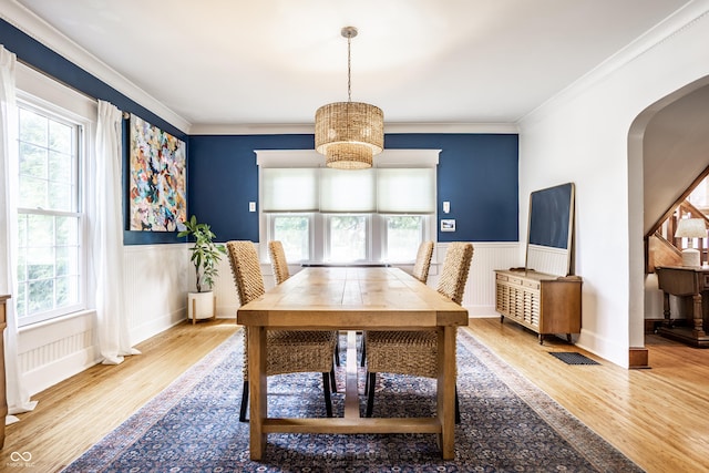 dining room featuring crown molding, an inviting chandelier, wainscoting, arched walkways, and wood finished floors