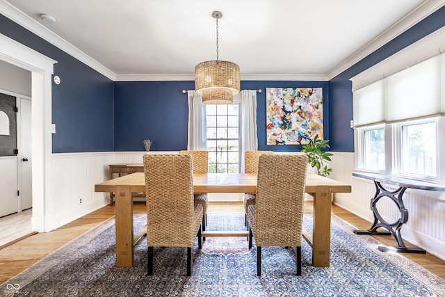 dining area with ornamental molding, wood finished floors, a notable chandelier, and a wainscoted wall