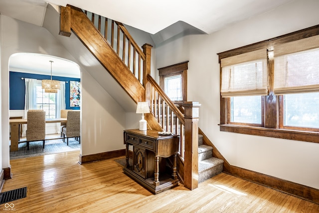 stairway with visible vents, wood finished floors, baseboards, arched walkways, and a notable chandelier