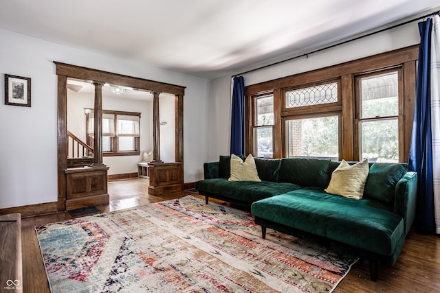 living area featuring baseboards, stairs, decorative columns, and wood finished floors