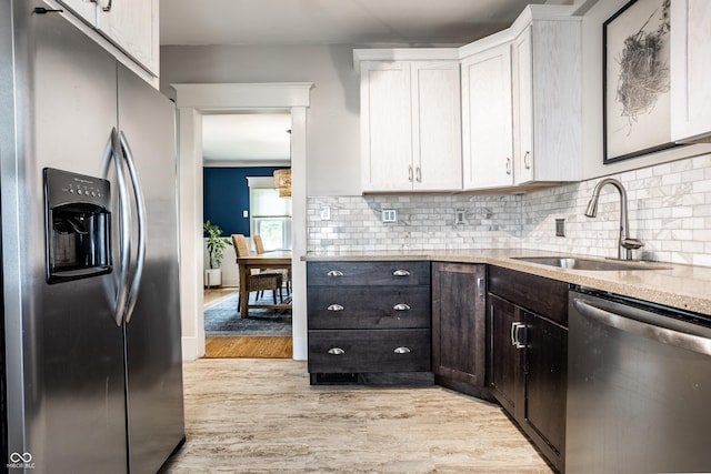 kitchen with white cabinets, a sink, stainless steel appliances, light wood-type flooring, and backsplash