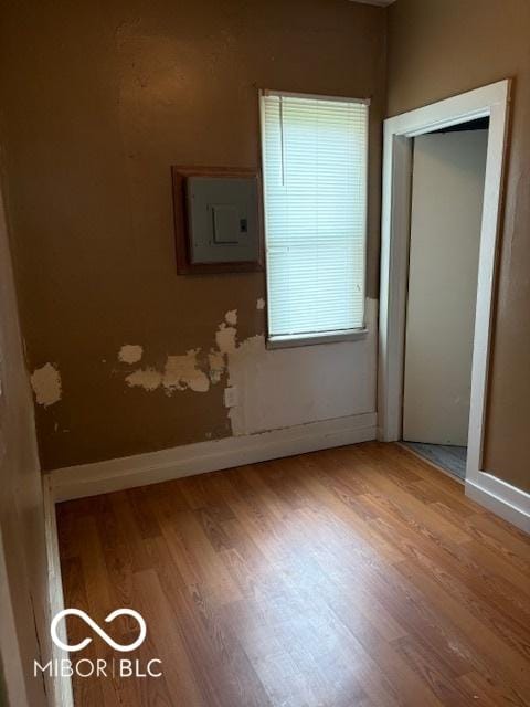 unfurnished bedroom featuring wood finished floors, a closet, electric panel, and baseboards