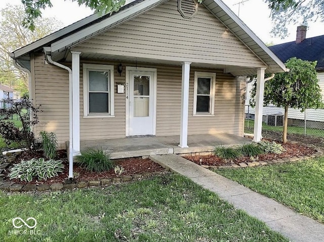 bungalow-style home with a front yard, covered porch, and fence