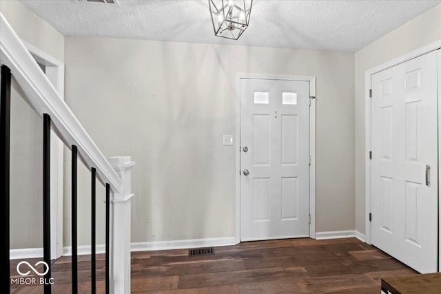 foyer featuring baseboards, a textured ceiling, visible vents, and wood finished floors