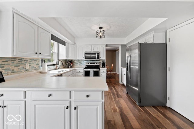 kitchen featuring dark wood-style flooring, appliances with stainless steel finishes, a sink, and a peninsula