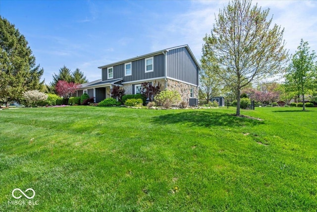 traditional-style home with central AC unit, board and batten siding, a front lawn, and stone siding
