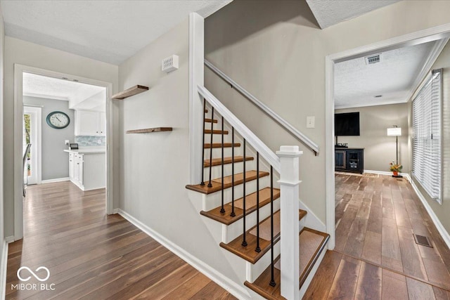 staircase with a textured ceiling, visible vents, baseboards, and hardwood / wood-style floors