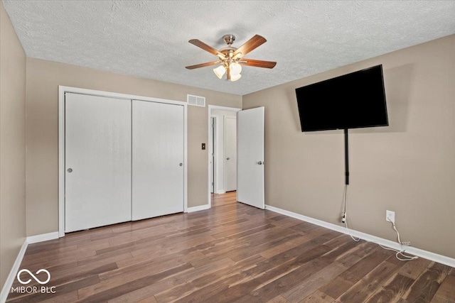 unfurnished bedroom featuring a textured ceiling, baseboards, wood finished floors, visible vents, and a closet
