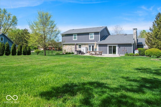 back of property featuring a patio, a chimney, a yard, and stone siding