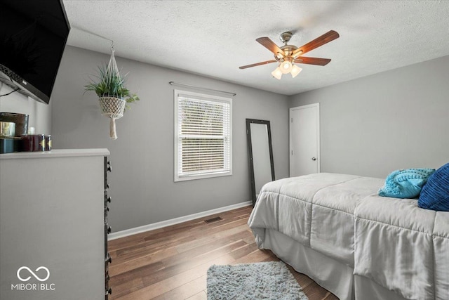 bedroom featuring ceiling fan, a textured ceiling, visible vents, hardwood / wood-style flooring, and baseboards