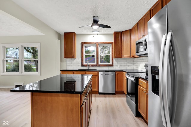 kitchen with appliances with stainless steel finishes, light wood-style floors, backsplash, and a sink