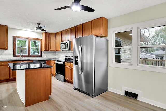 kitchen with appliances with stainless steel finishes, ceiling fan, backsplash, light wood finished floors, and a sink