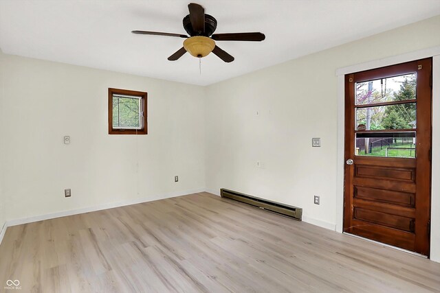 empty room featuring a wealth of natural light, ceiling fan, light wood-type flooring, and baseboard heating