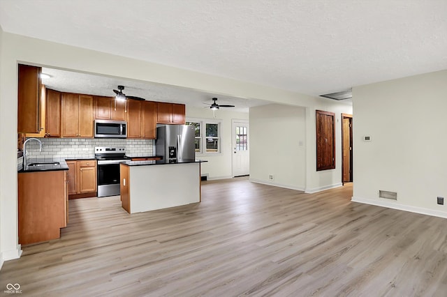 kitchen featuring appliances with stainless steel finishes, dark countertops, light wood finished floors, and a sink