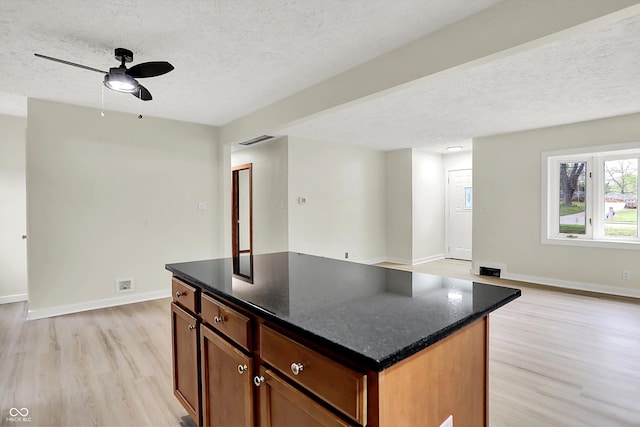 kitchen with light wood-style floors, a center island, visible vents, a textured ceiling, and open floor plan
