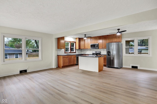kitchen with a textured ceiling, decorative backsplash, appliances with stainless steel finishes, light wood-style floors, and dark countertops