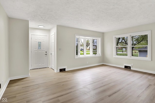 unfurnished living room with baseboards, light wood-type flooring, visible vents, and a textured ceiling