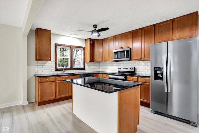 kitchen with brown cabinets, a sink, appliances with stainless steel finishes, light wood finished floors, and backsplash