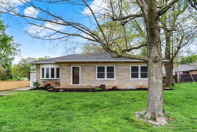 ranch-style house featuring fence, a shingled roof, a front yard, and stone siding