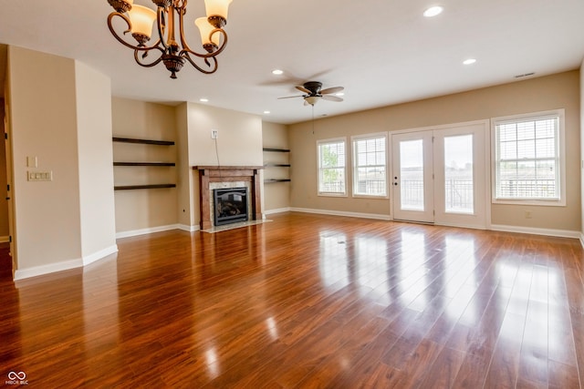 unfurnished living room featuring baseboards, a high end fireplace, ceiling fan with notable chandelier, and wood finished floors