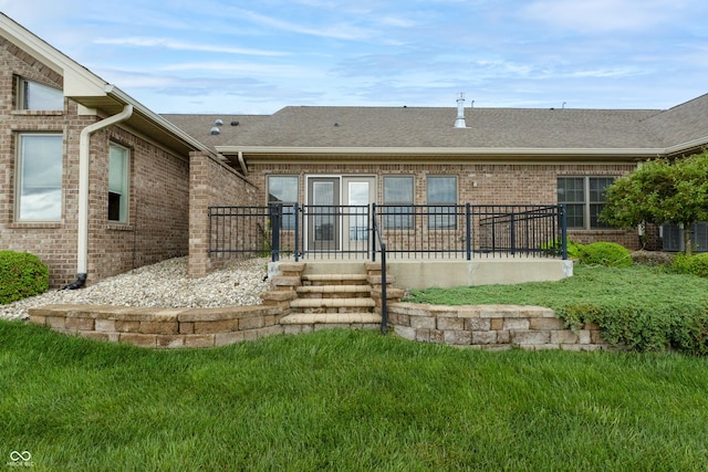 rear view of property with brick siding, a shingled roof, and a yard