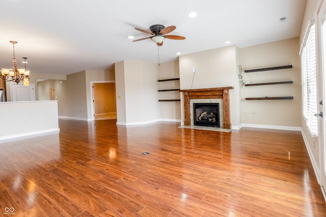 unfurnished living room with baseboards, a fireplace with flush hearth, light wood-style flooring, and ceiling fan with notable chandelier