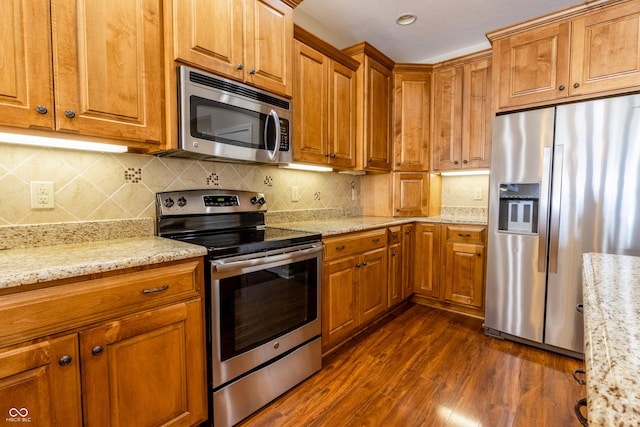 kitchen featuring dark wood-style flooring, appliances with stainless steel finishes, brown cabinetry, and light stone counters