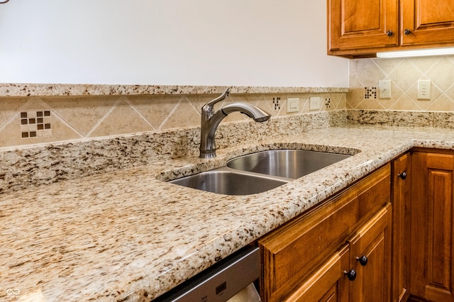 details featuring a sink, backsplash, brown cabinets, and light stone countertops