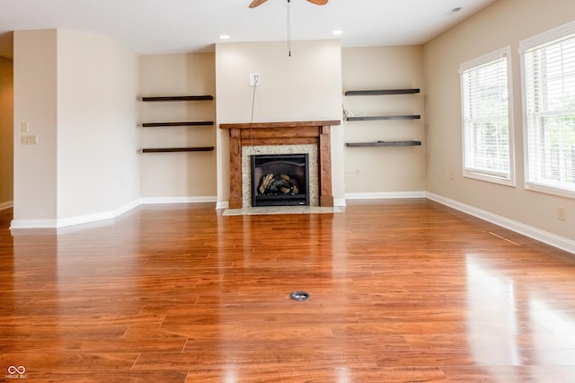 unfurnished living room with ceiling fan, built in features, baseboards, light wood finished floors, and a premium fireplace