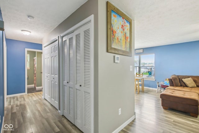 corridor with a textured ceiling, wood finished floors, and baseboards