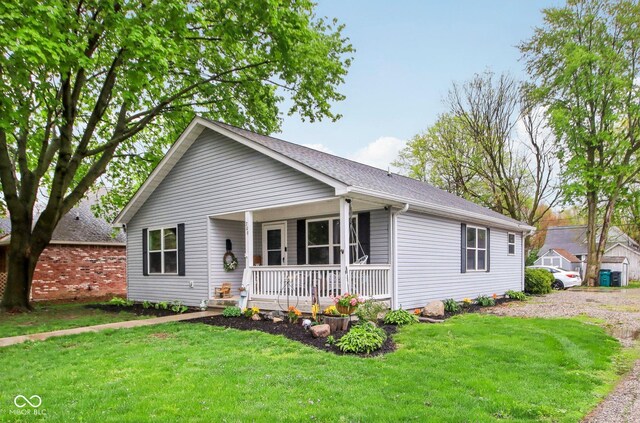 ranch-style house with a porch, a front yard, and roof with shingles