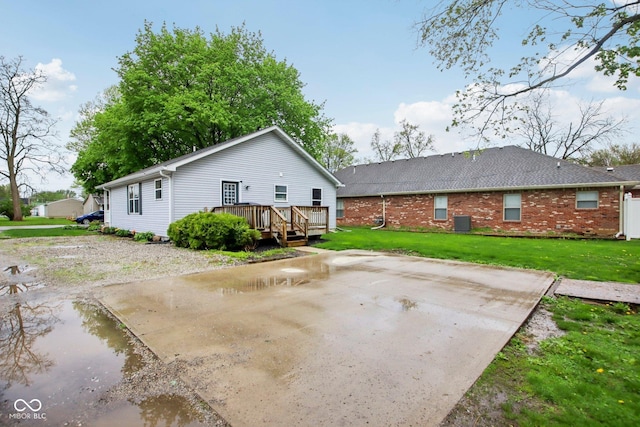 rear view of house with a deck, brick siding, a patio, central AC, and a lawn