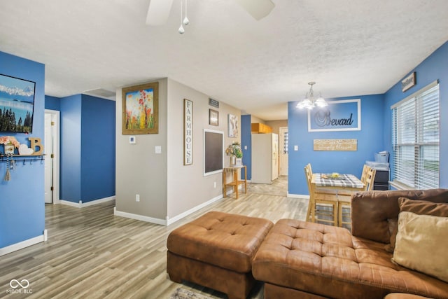 living area with wood finished floors, ceiling fan with notable chandelier, and baseboards