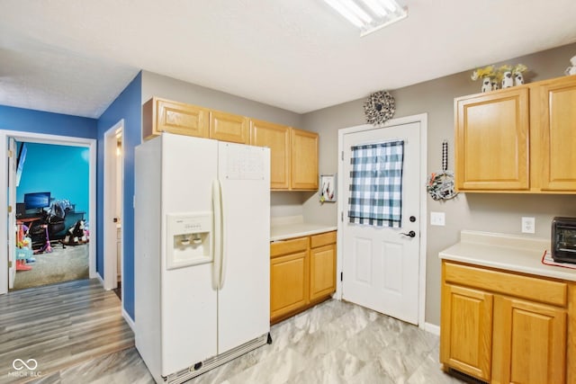 kitchen featuring white refrigerator with ice dispenser, light brown cabinets, light countertops, baseboards, and a toaster