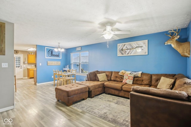 living area with baseboards, light wood-type flooring, ceiling fan with notable chandelier, and a textured ceiling