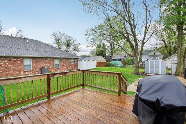 wooden terrace featuring an outdoor structure, a shed, a lawn, grilling area, and fence