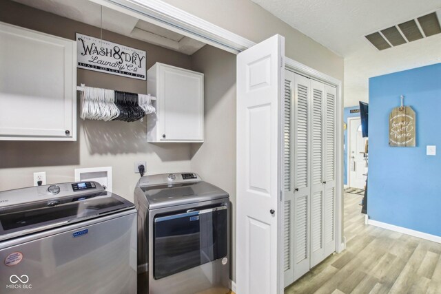 laundry room featuring washing machine and dryer, light wood finished floors, cabinet space, and visible vents