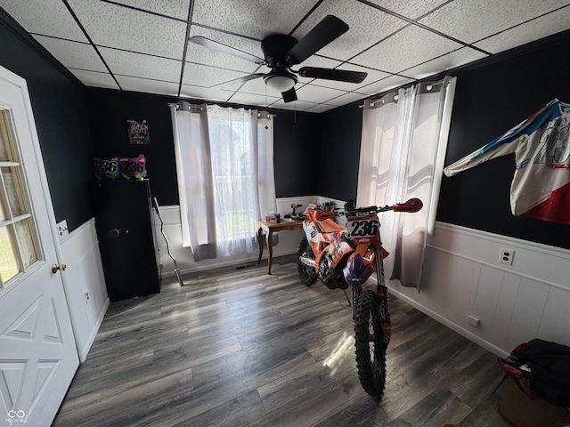 interior space with a ceiling fan, wainscoting, a paneled ceiling, and wood finished floors