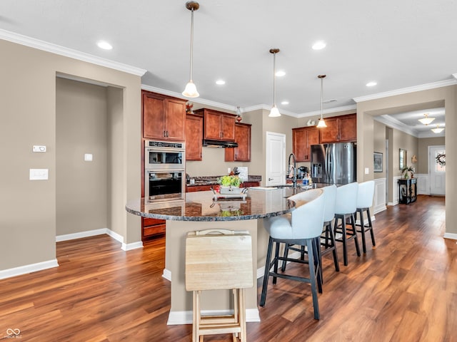 kitchen with a large island, under cabinet range hood, a kitchen breakfast bar, ornamental molding, and dark wood finished floors