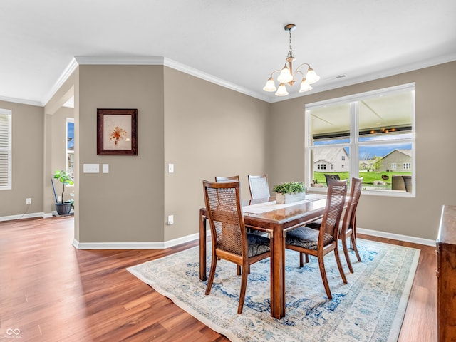 dining room featuring wood finished floors, a chandelier, ornamental molding, and baseboards