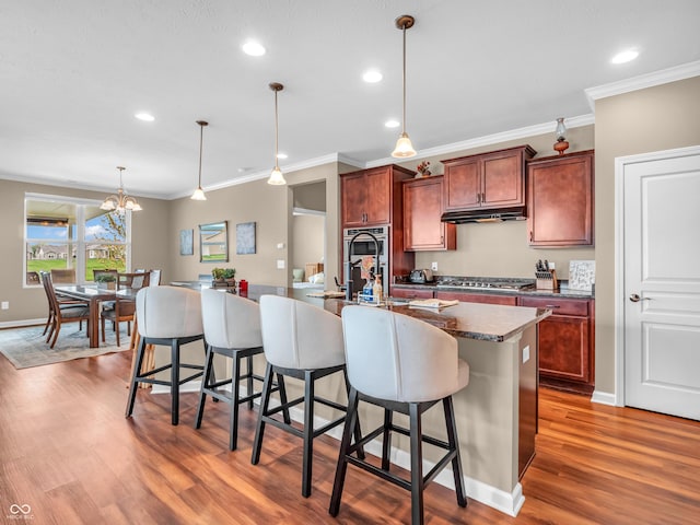 kitchen featuring wood finished floors, a breakfast bar, appliances with stainless steel finishes, pendant lighting, and crown molding