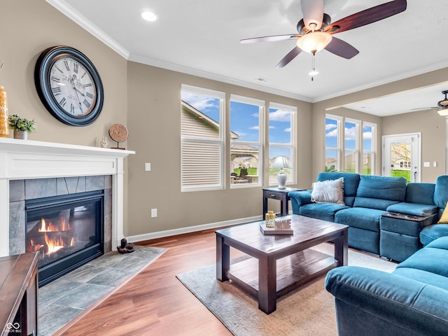 living area with crown molding, baseboards, light wood-type flooring, a fireplace, and a ceiling fan