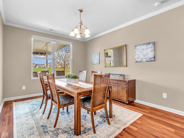 dining space featuring wood finished floors, crown molding, a notable chandelier, and baseboards